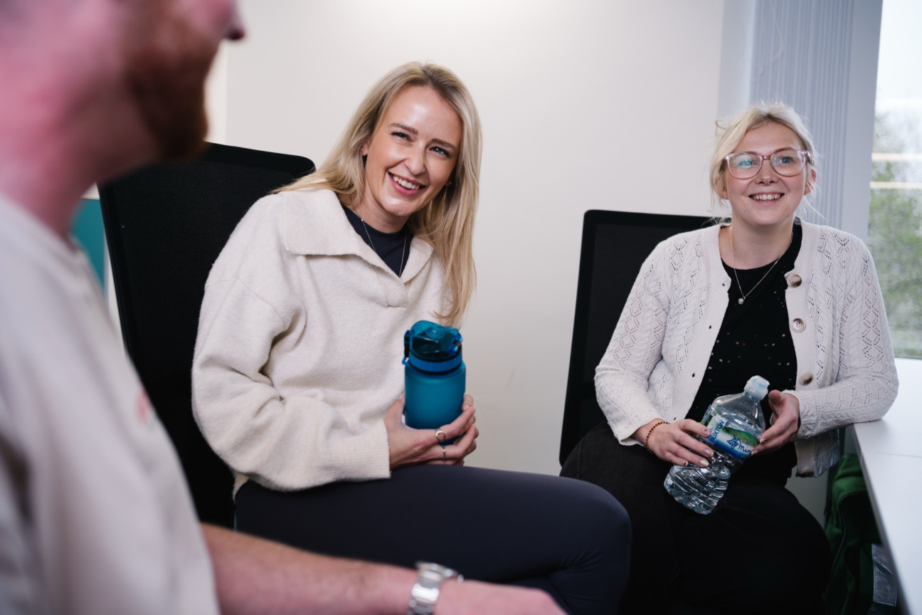 Three colleagues chatting together at desks with water bottles