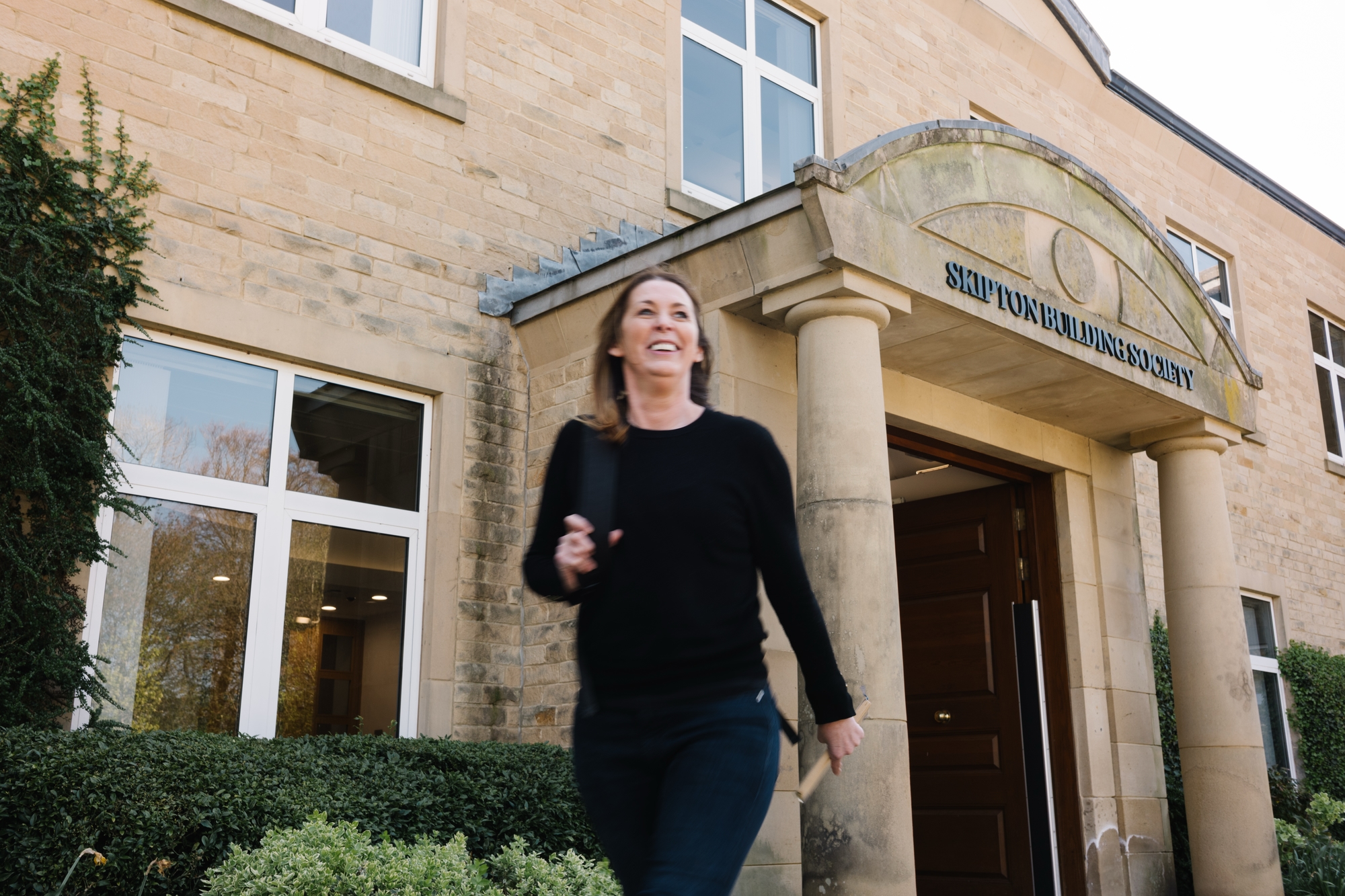 Colleague leaving Skipton Head Office with the front of the building in the background.