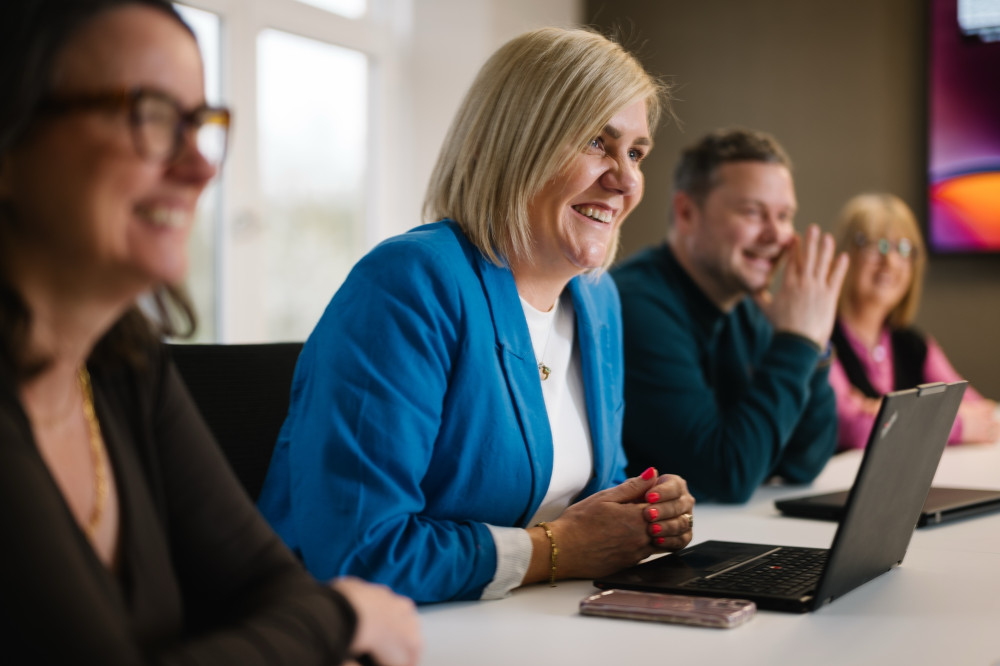 Colleague at laptop in blue jacket smiling in meeting.