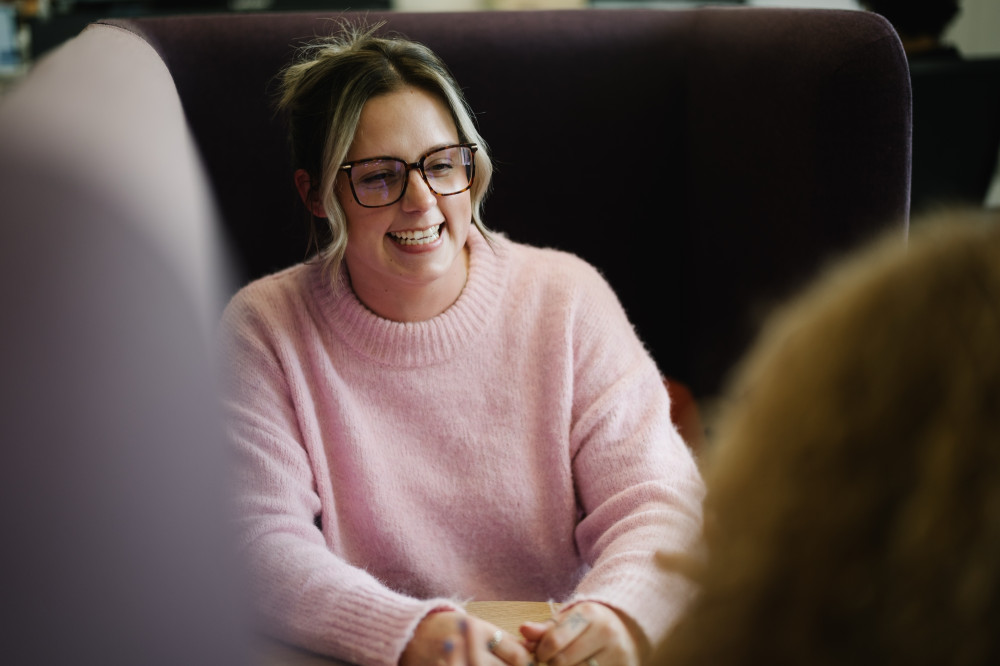 Colleague in glasses and pink jumper smiling in meeting.