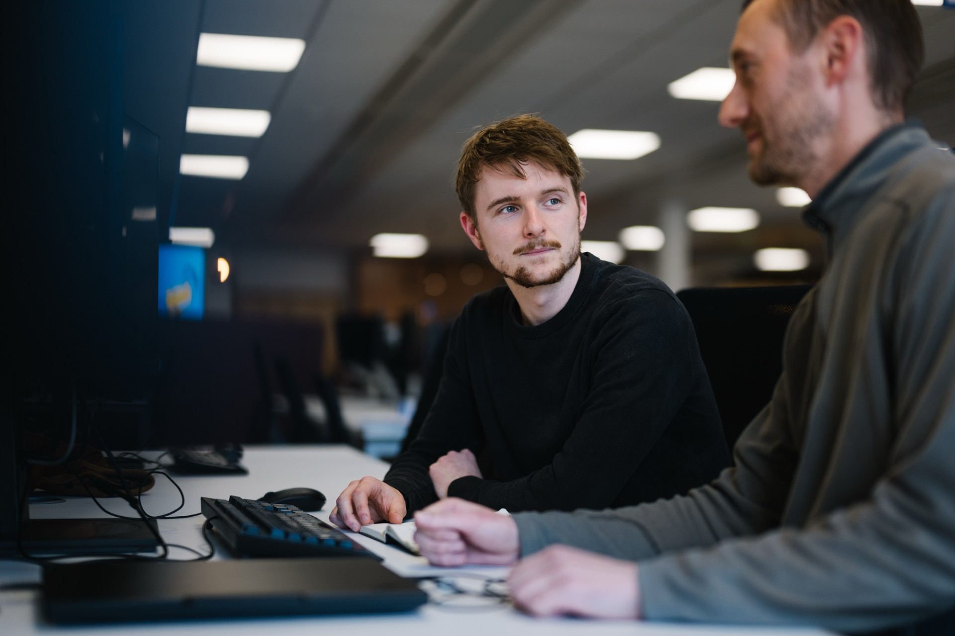 Male colleagues working at computer desk together.